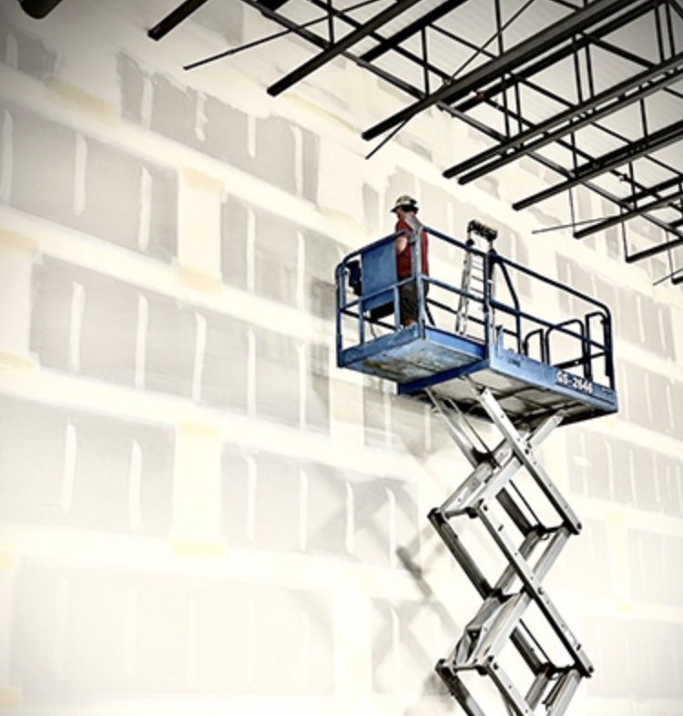 Drywall finisher on a scissor lift finishing a tall commercial wall